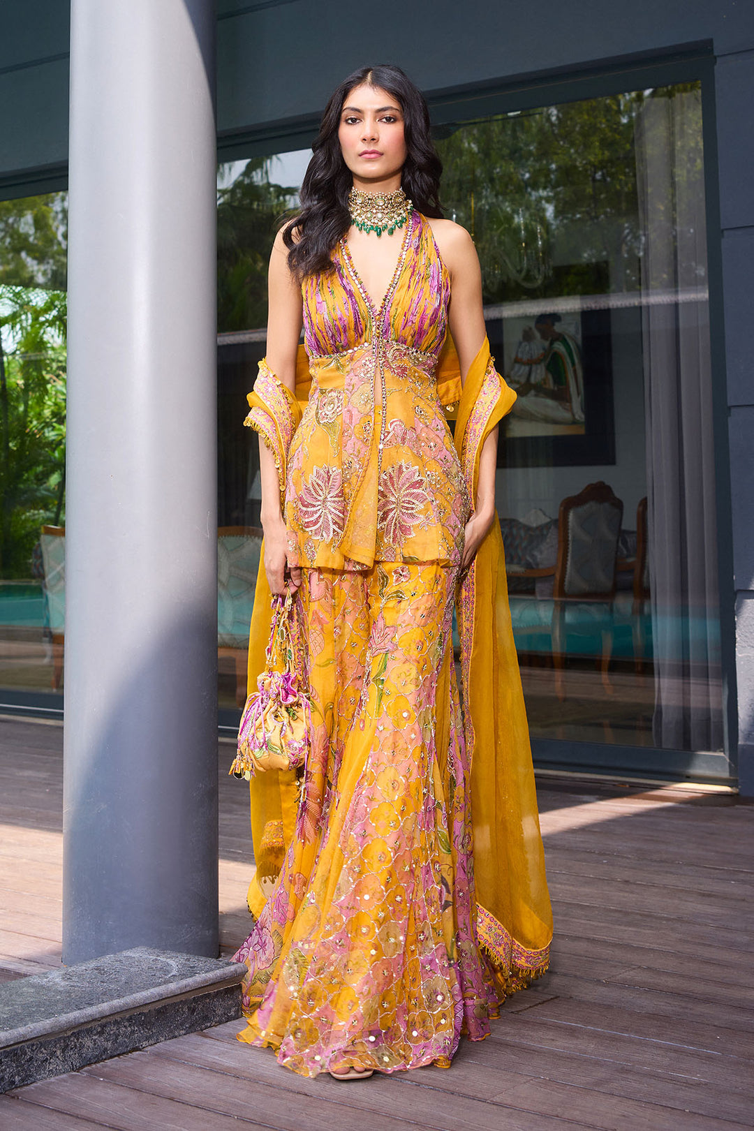 Woman in a yellow floral dress standing outdoors near a building entrance.
